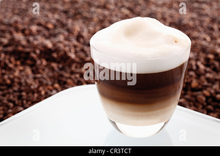 Cappuccino in a glass on a tray in front of coffee beans Stock Photo