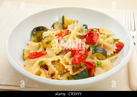 A bowl of pasta bows or farfalle with roast courgettes or zucchini, red pepper and tomato with olive oil and herbs. Stock Photo