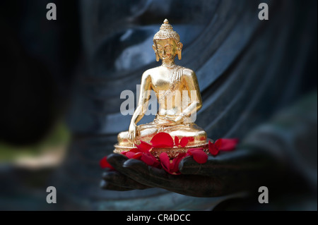 Golden Buddha statue and red rose petals on the hand of a very large buddha statue Stock Photo