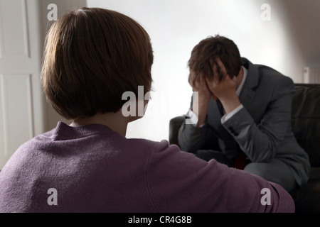 Back view of female looking at a man with his head in his hands. Both unrecognisable. Stock Photo