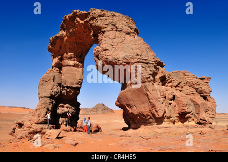 Tourists below the rock arch or natural bridge of In Tehak, Acacus Mountains or Tadrart Acacus range Stock Photo