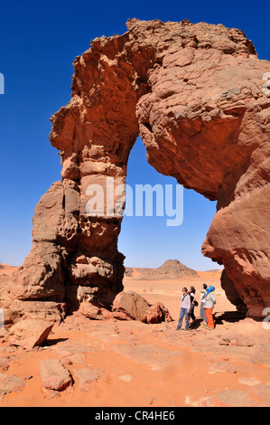 Tourists below the rock arch or natural bridge of In Tehak, Acacus Mountains or Tadrart Acacus range Stock Photo
