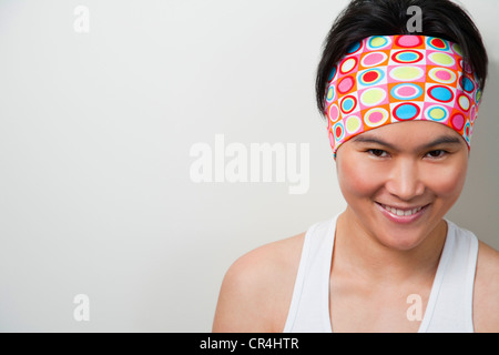 Portrait of young healthy looking asian woman wearing white sleeveless top looking at camera and smiling Stock Photo