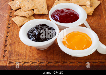 Selection of jams with crisp biscuits for tasting on an old wooden board. Blackcurrant jam, strawberry jam, lemon curd. Stock Photo