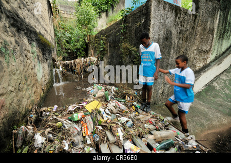 Residents of the slum district of Favela Morro da Formiga standing beside waste in an exposed sewer canal, Tijuca district Stock Photo