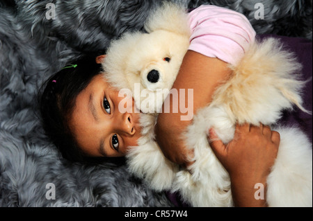Girl with indigenous facial features hugging a teddy bear, production of soft toys and carpets from alpaca fur in a small family Stock Photo