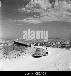 South Africa,1950s. Female tourist stops her car on a dusty, gravel road in the outback. Stock Photo