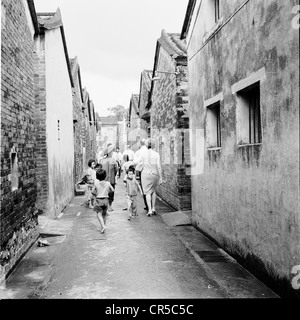 Historical picture from Hong Kong,1950s. A western couple walk the back streets followed by local chinese children. Stock Photo