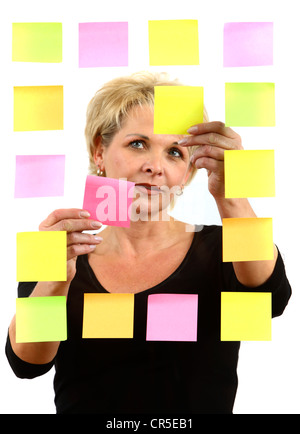 woman sticks self-adhesive sticky notes, paper notes, stuck to a pane of glass. Different colors. Stock Photo