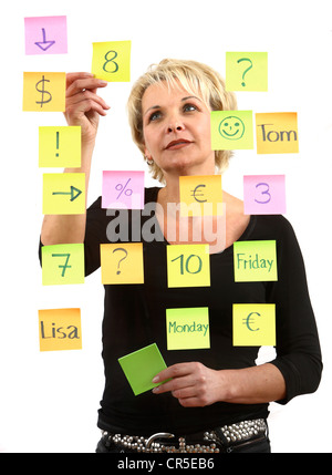 woman sticks self-adhesive sticky notes, paper notes, stuck to a pane of glass. Different colors. Stock Photo