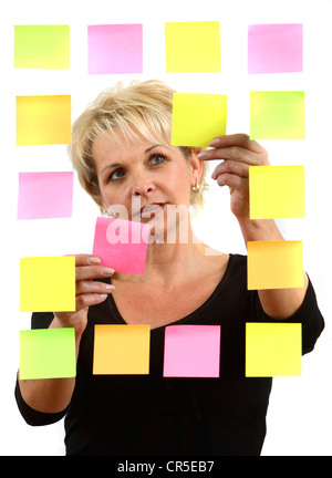 woman sticks self-adhesive sticky notes, paper notes, stuck to a pane of glass. Different colors. Stock Photo