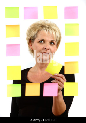 woman sticks self-adhesive sticky notes, paper notes, stuck to a pane of glass. Different colors. Stock Photo