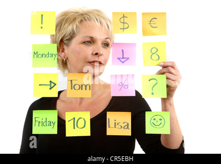 woman sticks self-adhesive sticky notes, paper notes, stuck to a pane of glass. Different colors. Stock Photo