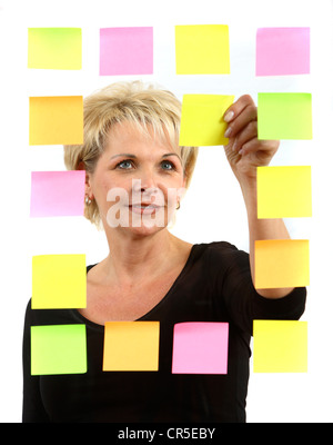 woman sticks self-adhesive sticky notes, paper notes, stuck to a pane of glass. Different colors. Stock Photo