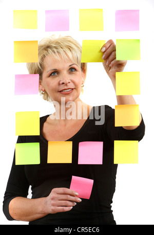 woman sticks self-adhesive sticky notes, paper notes, stuck to a pane of glass. Different colors. Stock Photo