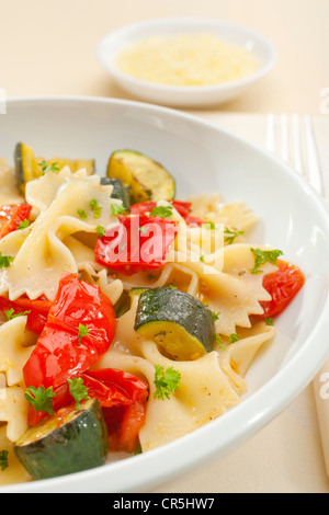 A bowl of pasta bows or farfalle with roast courgettes or zucchini, red pepper and tomato with olive oil and herbs. Stock Photo