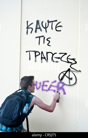 'Burn the banks' graffiti and participant in the Athens, Greece gay parade adding with spray ' queer' Stock Photo