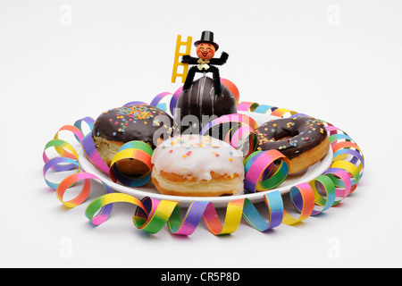 Doughnuts and glaced filled doughnuts on a plate with New Year's decorations, a garland and a chimney sweep Stock Photo