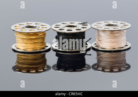 close up of three sewing machine bobbins with different colour threads with reflections Stock Photo