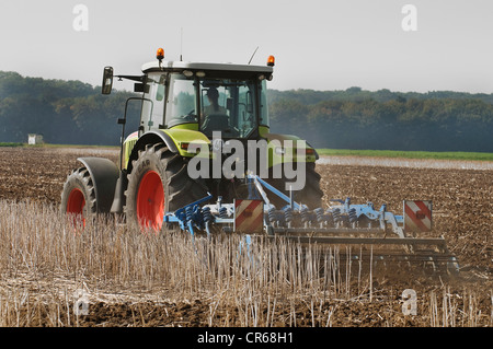 Tractor with a cultivator driving on a harvested field, soil is being stirred and pulverized, remains of plants are being Stock Photo