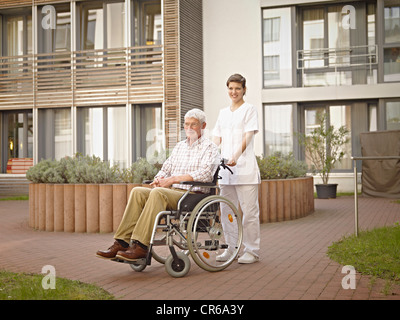 Germany, Cologne, Caretaker pushing senior man in wheelchair outside of nursing home Stock Photo