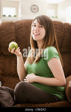 Portrait of pregnant woman sitting on sofa and eating apple