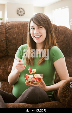 Portrait of pregnant woman sitting on sofa and eating salad