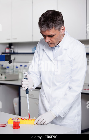 Germany, Bavaria, Munich, Scientist pouring red liquid with pipette in test tube for medical research in laboratory