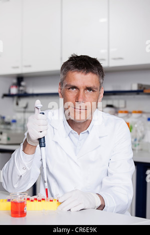 Germany, Bavaria, Munich, Scientist pouring red liquid with pipette for medical research in laboratory