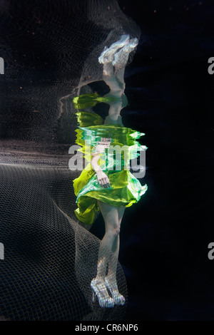 Caucasian woman in dress swimming under water