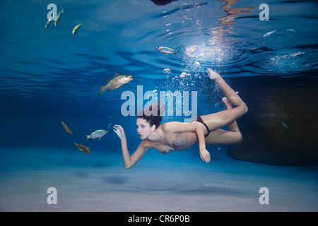 Mixed race woman swimming in water with fish Stock Photo