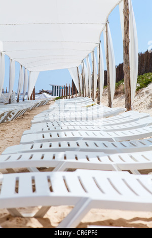Line from white plastic lounges in sandy beach under big parasol. Monastir, Tunisia Stock Photo