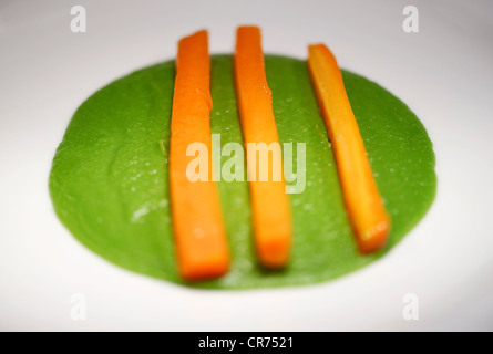 chopped carrot sticks in lines on a bed of mushy peas on a white plate in a restaurant Stock Photo