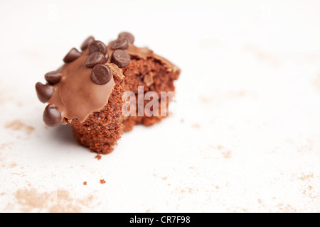 A chocolate cupcake with a bite out of it, surrounded by a dusting of cocoa powder Stock Photo