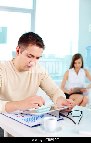 Serious businessman working with digital tablet at workplace with his colleague on background Stock Photo