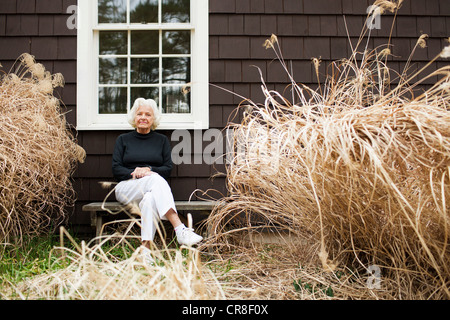 Portrait of senior woman sitting on bench outside house Stock Photo