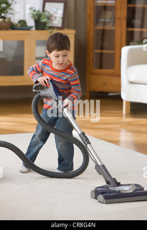 Boy using vacuum cleaner on rug Stock Photo