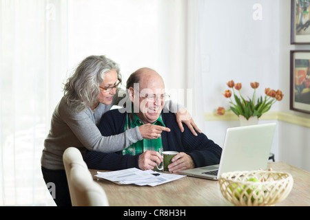 Senior couple using laptop at home, laughing Stock Photo