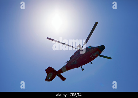 Coast Guard helicopter flying past the sun on a clear day Stock Photo