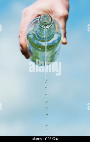 Pouring drinking water from a glass bottle against a blue sky Stock Photo