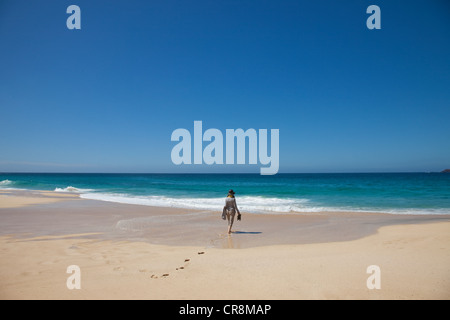 Woman alone on a beach, walking toward the sea Stock Photo