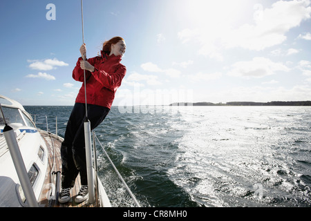 Woman stands holding rope on deck of sailing yacht, nautical fashion