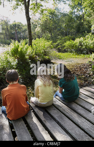 Three children sitting on boardwalk in forest