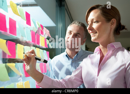 Two businesspeople writing on adhesive notes on window Stock Photo