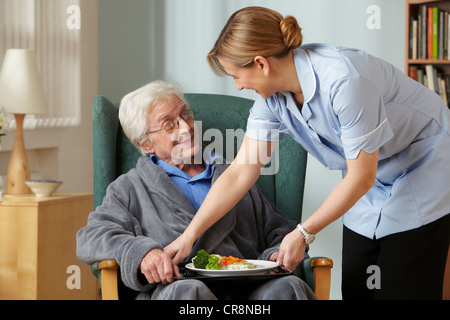 Carer bringing meal to senior man Stock Photo