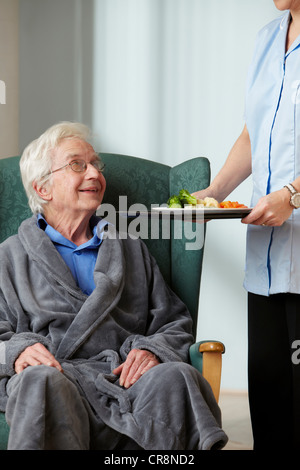 Carer bringing meal to senior man Stock Photo