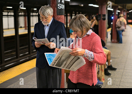 Woman reading New York Times Book Review next to man reading magazine on New York City subway platform, Manhattan, New York Stock Photo