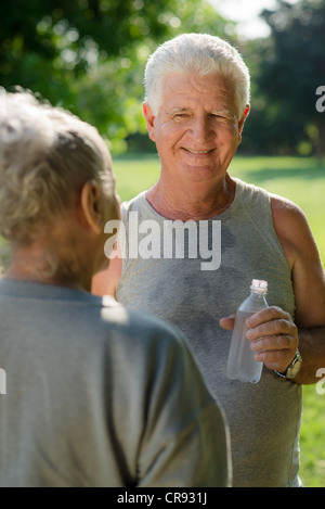 Senior people, old man and woman talking and drinking water after exercising in park Stock Photo