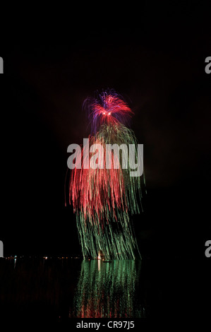 Aerial fireworks display on the lake, rockets forming waterfall, green and red light trails with reflections, Schliersee Lake Stock Photo