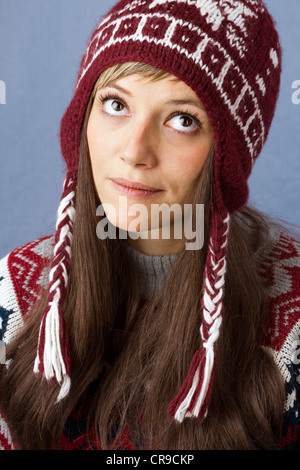 Pretty young woman wearing pullover and wool cap with looks up annoyed. Funny portrait against a light blue background Stock Photo